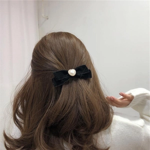 Elegant black velvet bow hair clip with heart pearl shown on model's wavy brown hair