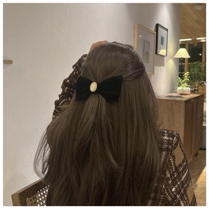 Detailed view of a black velvet bow hair clip with a vintage pearl center on hair