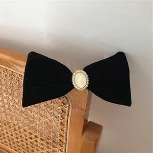 French vintage black velvet bow hair clip with central pearl on a rustic wooden chair
