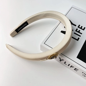 Detail view of champagne satin headband featuring vintage metal crest and handmade label