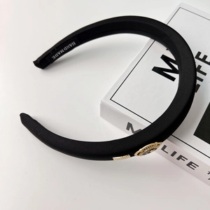 Close-up of elegant black fabric headband with golden emblem and handmade label detail