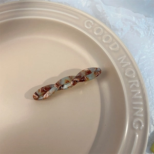 Detailed view of twist-design acetate hair clip with brown and blue marble texture