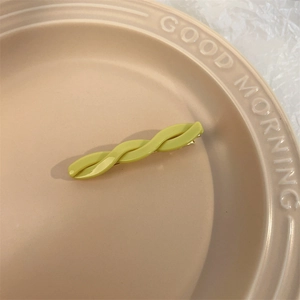 Detail of fruit green wavy cellulose hair clip on a beige plate with high glossy finish