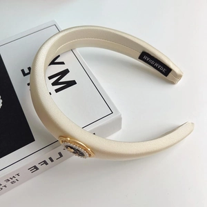 Elegant champagne satin padded headband with decorative black and gold emblem for women