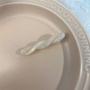 Detailed view of white pearlescent twisted acetate hair clip on a ceramic tray