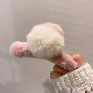 Gros plan d'une pince à cheveux en peluche rose avec un pompon en fourrure blanc crème