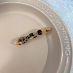 Close-up of a twisted acetate hair clip with tortoise shell texture on a ceramic dish