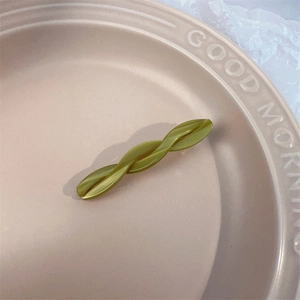 Detailed view of an olive green twisted acetate hair clip on a pink ceramic plate