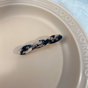 Detailed top view of twisted acetate hair clip with tortoiseshell texture on a ceramic plate
