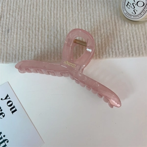 Détail d'une grande pince à cheveux en résine rose avec inscription dorée sur fond doux