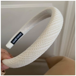 Close-up of beige knitted wide headband with diagonal texture and hand made label detail