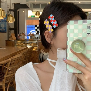 Detail of wavy checkerboard hairpins in purple and red worn by a model in a cozy cafe