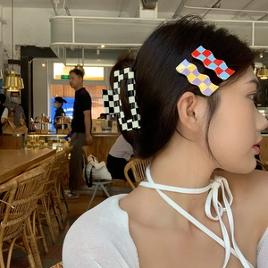Detail showing a checkered hair claw and wave clips worn on a model in a cozy cafe