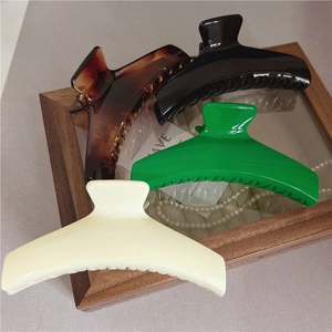 Dettaglio di quattro grandi mollette per capelli in nero, crema, verde e tartarugato