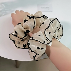 Détail d'un chouchou en organza beige clair avec motifs cœurs noirs et bordure contrastée