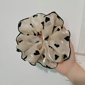 Gros plan d'un grand chouchou en satin crème avec motifs cœurs noirs et bords ondulés