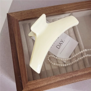 Dettaglio di una grande pinza per capelli giallo crema minimalista con finitura lucida