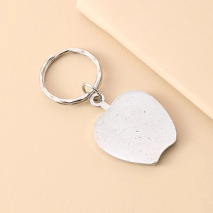Minimalist silver alloy apple keychain pendant with a smooth matte finish on a beige surface