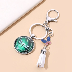Silver dragonfly keychain with purple butterfly charm and white tassel on pink background