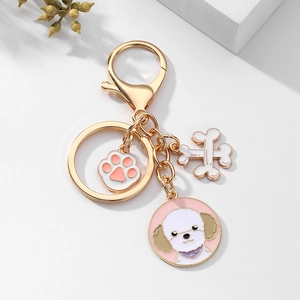 Détail d'un porte-clés doré pour chien avec breloques bichon, patte rose et os mignon