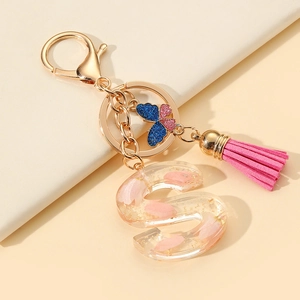 Detail of resin letter S keychain with pink petals, gold flakes, and a suede tassel