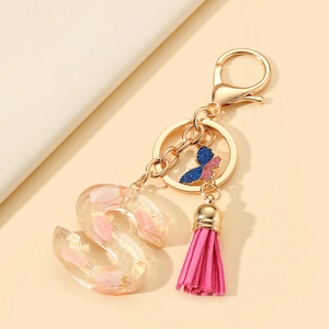Detail of resin letter S keychain with pink petals, gold foil, butterfly and tassel