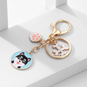 Détail d'un porte-clés doré avec Shiba Inu, patte rose et pendentif d'os de chien