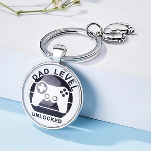Silver Dad Level Unlocked keychain with game controller icon and small baby feet charm