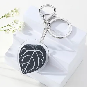 Detailed view of leaf-shaped acrylic keychain on white pedestal with baby's breath flowers