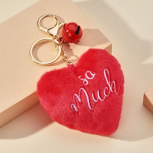 Détail d'un porte-clés en peluche cœur rouge avec cloche dorée et broderie so Much