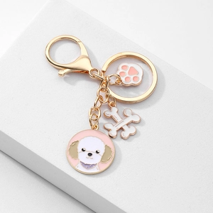 Détail d'un porte-clés doré avec pendentifs caniche rose, os blanc et patte mignonne