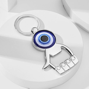 Porte-clés décapsuleur en métal argenté avec œil bleu sur un support minimaliste blanc