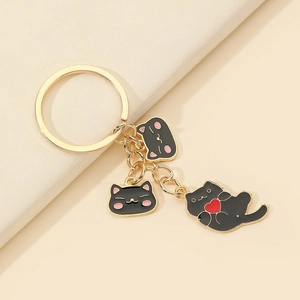 Détail de porte-clés chat avec anneaux dorés et breloques émaillées sur blocs beiges