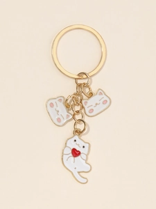 Détail d'un porte-clés doré avec trois chats en émail blanc et un pendentif cœur