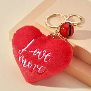 Détail de porte-clés cœur en peluche rouge avec broderie love more et clochette dorée