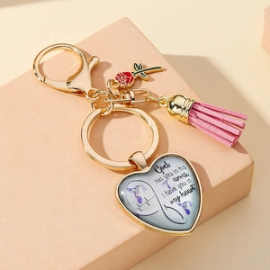 Macro detail of heart keychain with pink tassel, rose charm, and memorial text engraving