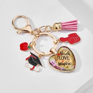 Close-up of golden graduation keychain with pink tassel and teach love inspire heart charm