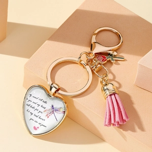 Detail of heart pendant keychain with pink tassel and dragonfly charm on gold metal