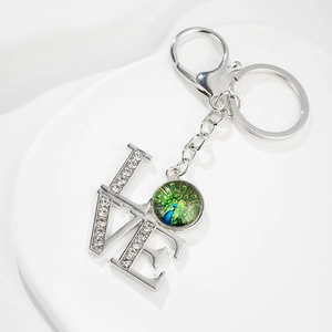 Close-up of LOVE keychain with peacock gem pendant and rhinestones on a white stand