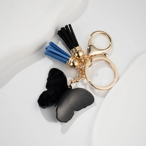 Blue butterfly keychain with black tassel and golden ring on a white stone pedestal