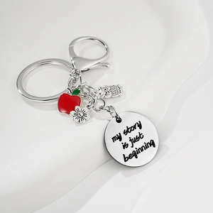 Détail macro du porte-clés en acier argenté avec pomme rouge et pendentifs gravés