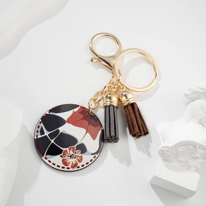 Detail of round leather keychain with geometric pattern and dual decorative tassels