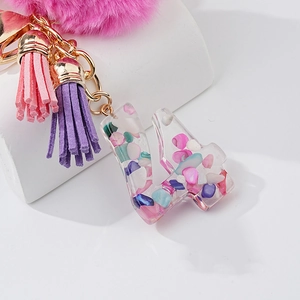 Détail macro du porte-clés pompon rose avec lettre en résine et chaîne dorée
