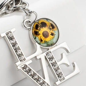 Silver LOVE keychain with sparkling rhinestones and a sunflower pendant on white surface