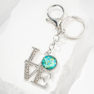 Sparkling LOVE keychain with diamond-set letters and artistic flower pendant on white stone