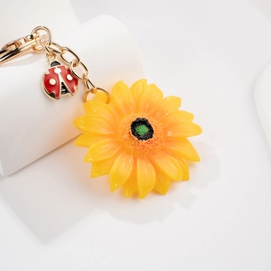 Dettaglio portachiavi a girasole 3D con piccola coccinella rossa e catena placcata oro