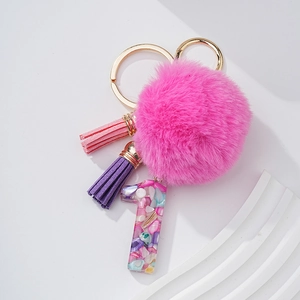 Détail d'un pompon fuchsia et de glands violets sur un porte-clés doré en forme de un