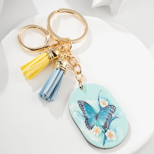 Detail of golden metal keychain with blue butterfly pendant and two colored tassels