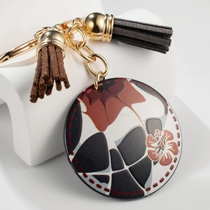 Geometric round pendant keychain with floral texture and tassels on white display stand
