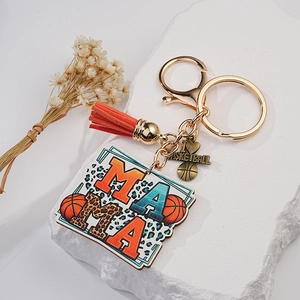 Detail of basketball keychain with MAMA charm and orange tassel on a white pedestal